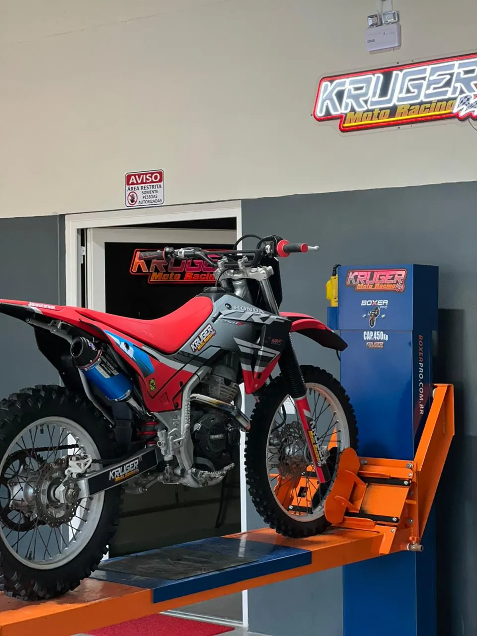 CRF 250F no elevador com o letreiro neon da Kruger
